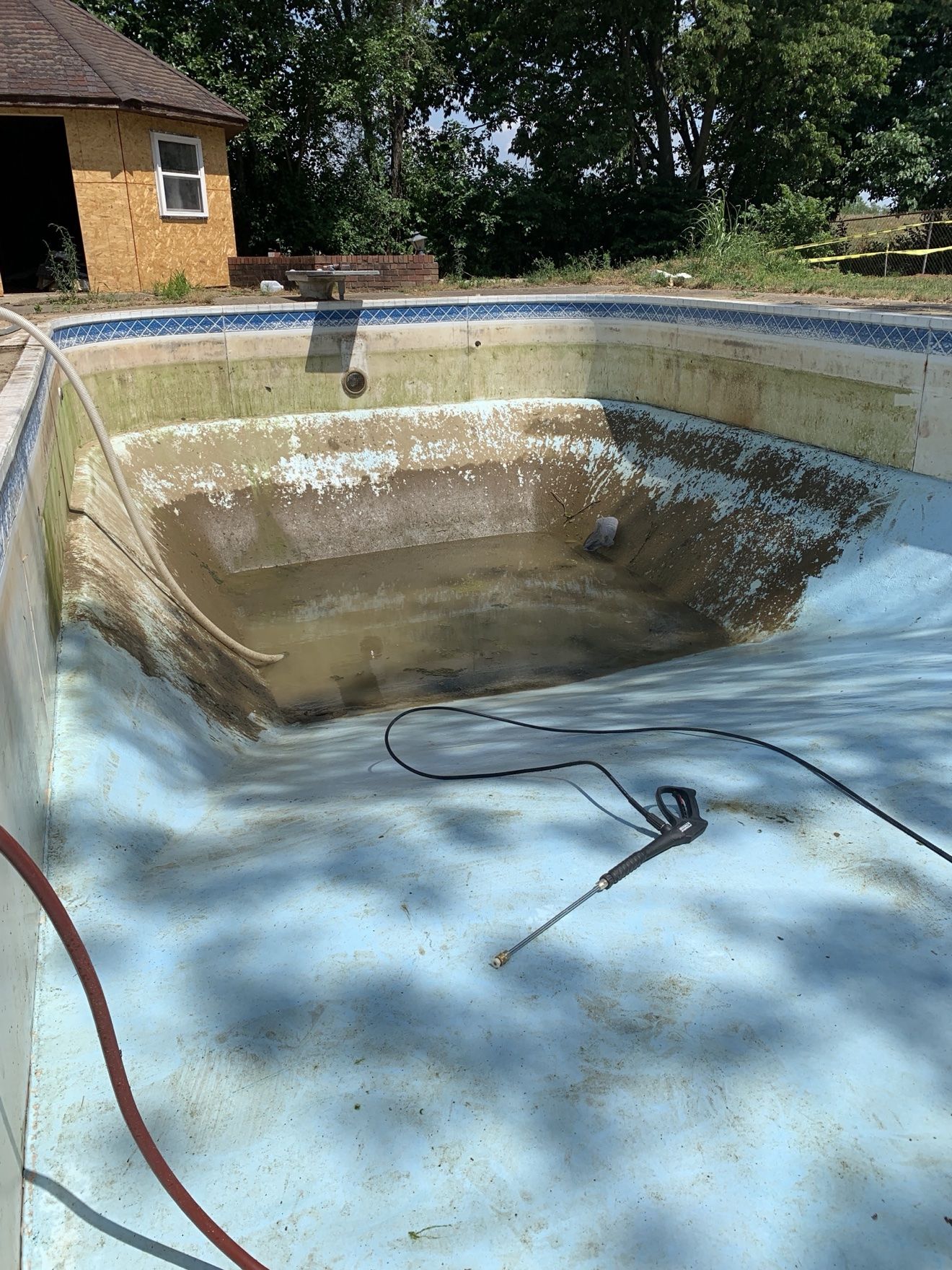 Inground pool drained before a liner replacement, old surface stained and peeling with a pressure washer in the pool