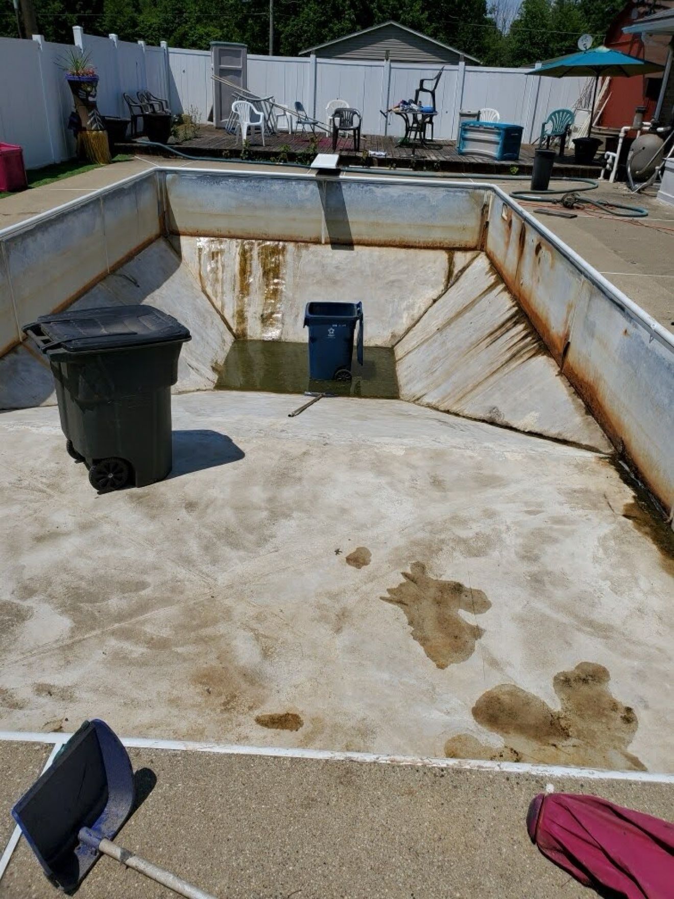 Pool with the old liner out, showing rust-stained steel walls and a stained floor