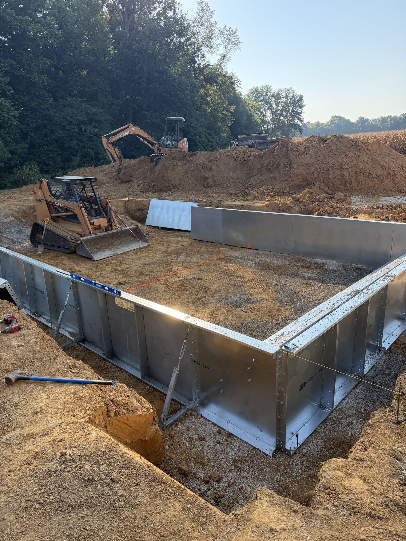 Steel wall panels going up on an inground pool build, skid steer working inside the pool